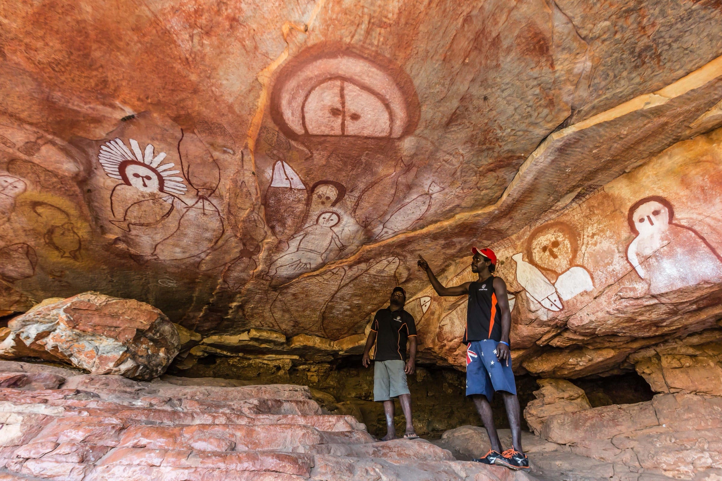 Two men observe ancient paintings on cave walls depicting simple humanoid figures
