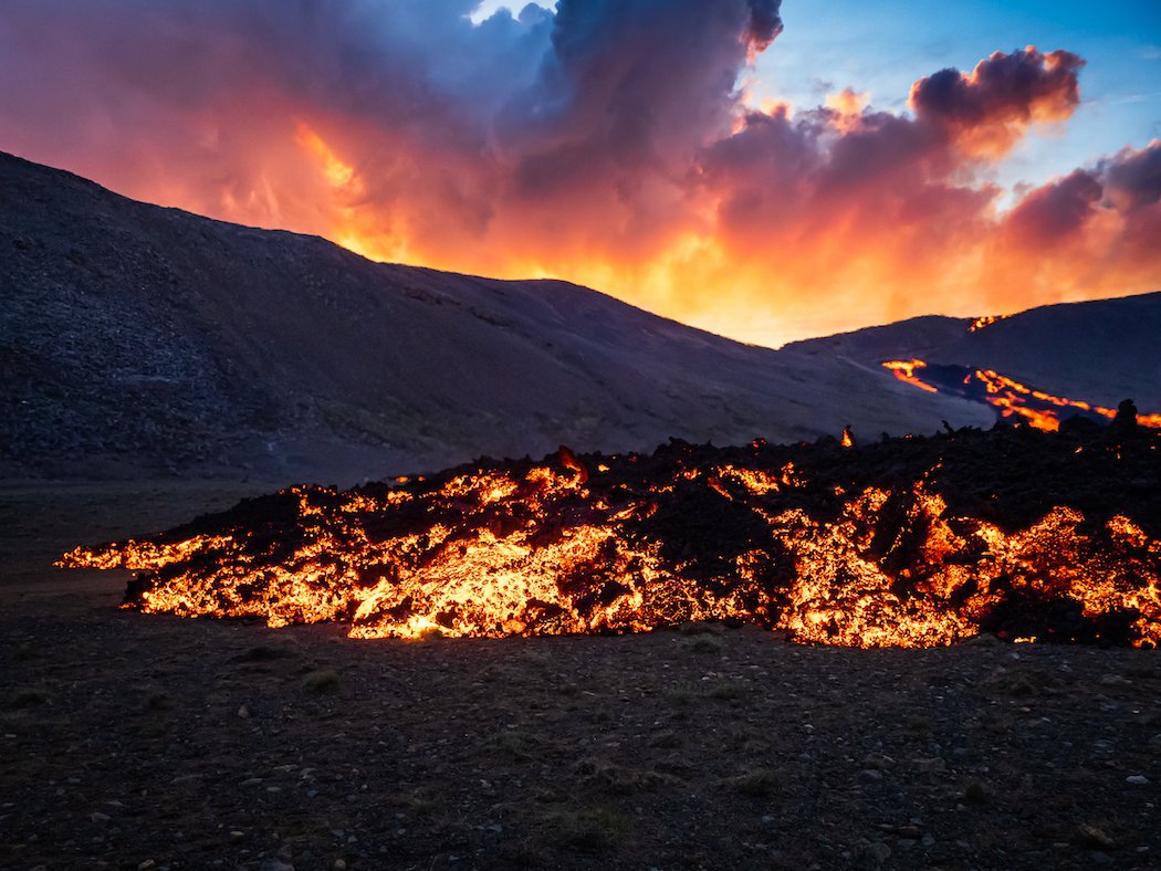 A volcanic gas cloud blooms over a river of lava in Iceland