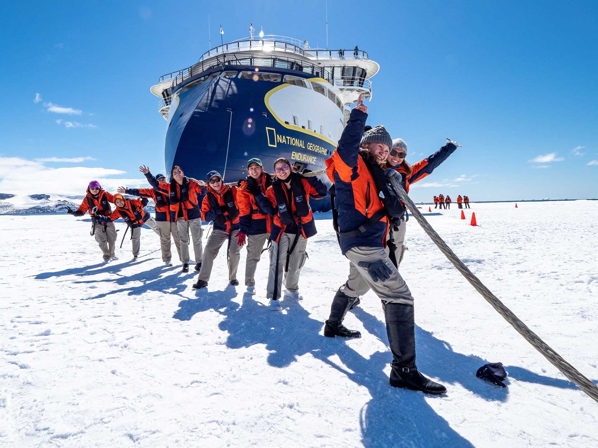 crew members in orange parkas pulling a rope attached to a ship